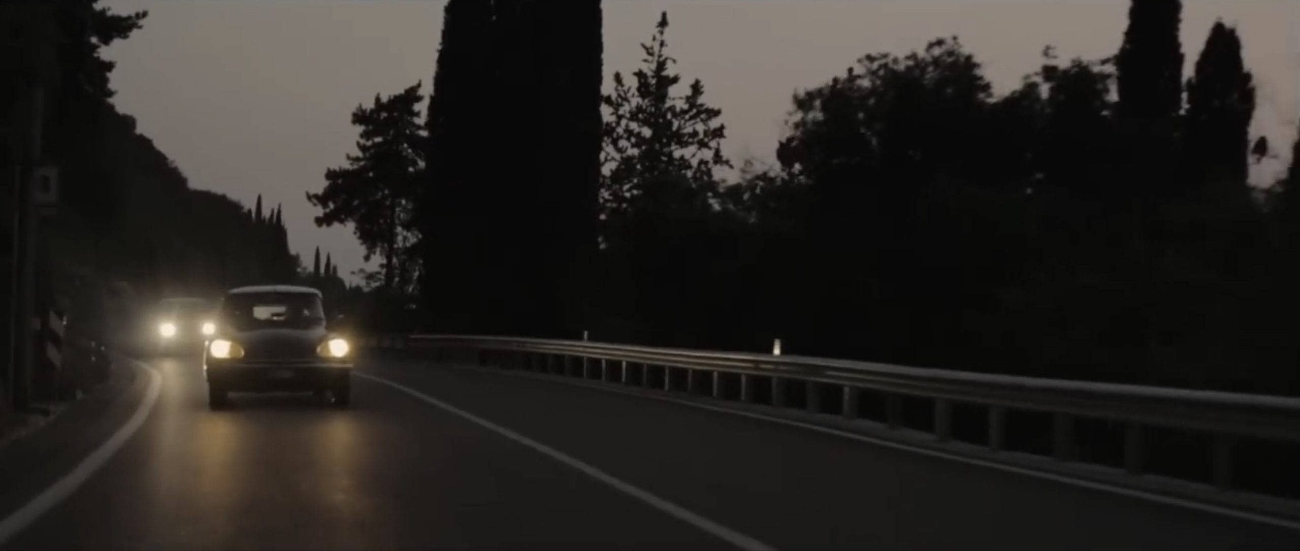 una Citroën squalo percorre una strada alberata di sera con i fari accesi, nel fotogramma di un video dei Virginiana Miller